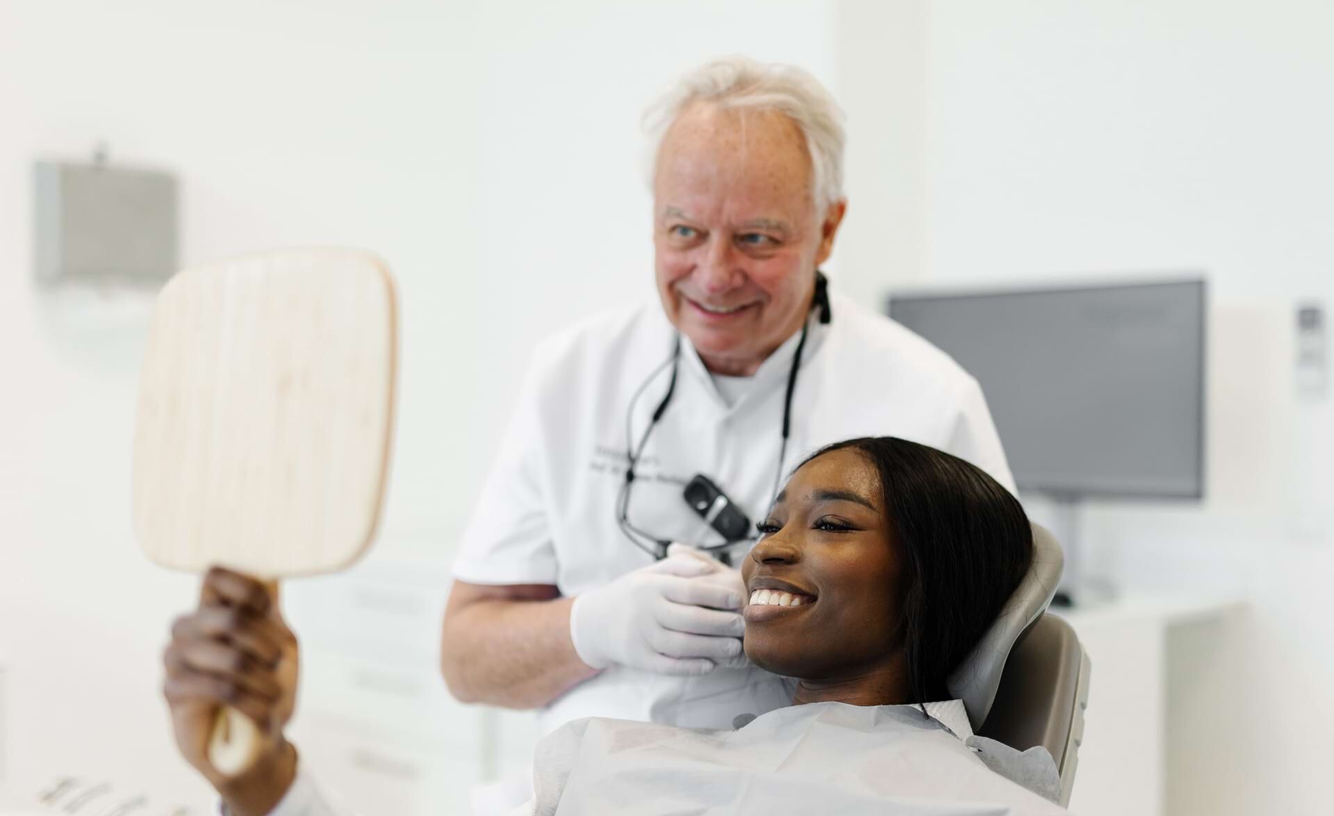 Situationsfoto einer lächelnden Patientin, die in einen Handspiegel schaut und Prof. Dr. med. dent. Hannes Wachetl